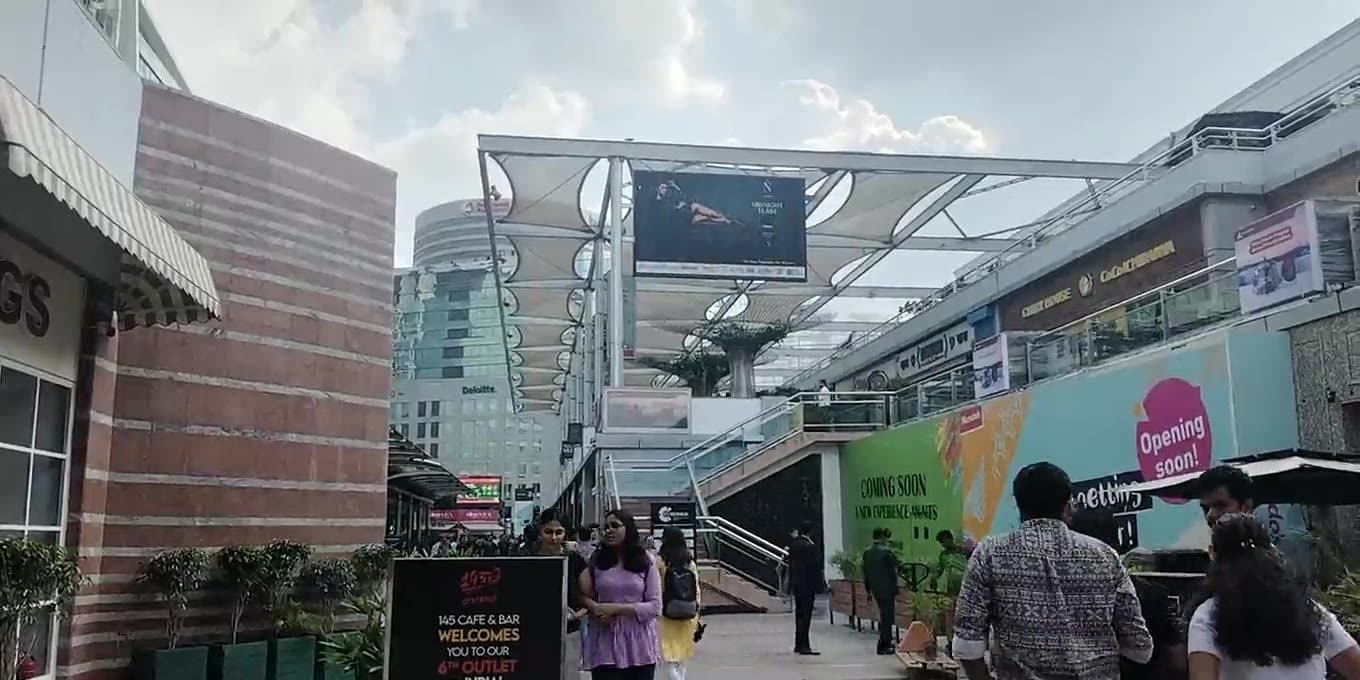 A glass office tower above a pedestrian plaza at an Indian commercial hub
