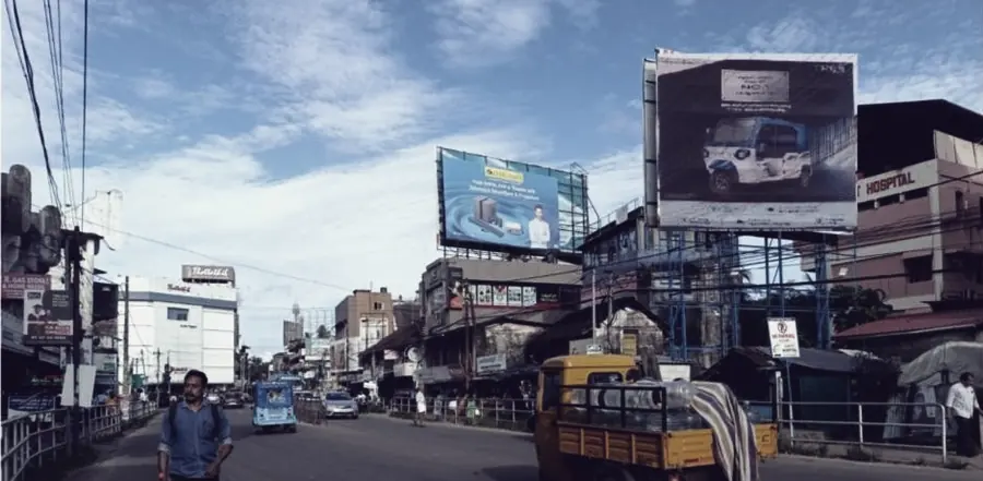 A pedestrian crossing a Kozhikode street beside stacked retail frontage