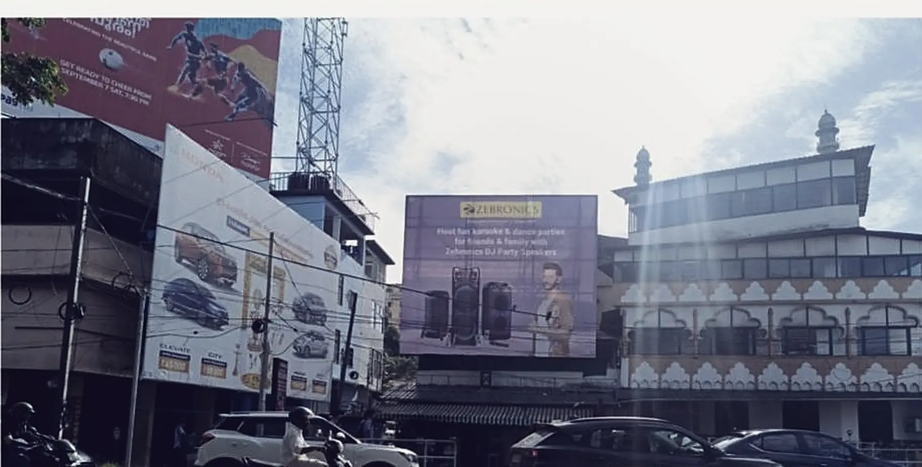A commercial building in Kozhikode carrying three large advertising panels across its face, traffic passing below