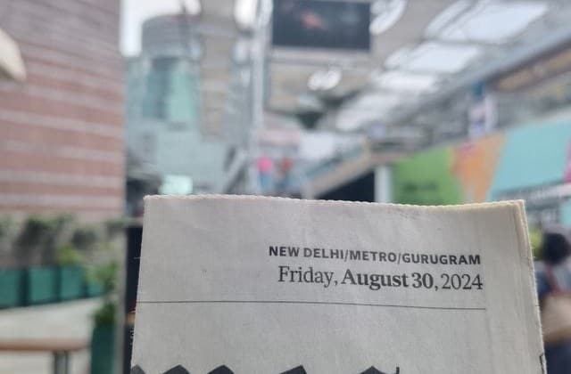 Digital screen at Cyber Hub photographed alongside that morning's newspaper as proof of the run date