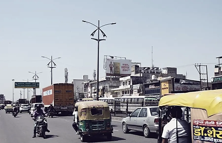 A wide road through Agra with a hoarding on the central median